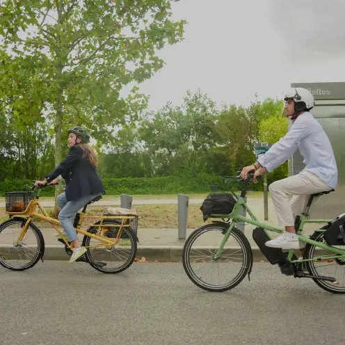 Femme sur un vélo cargo électrique jaune Yükargo accompagnée d’un homme sur un vélo cargo vert en ville, illustrant l’expérience Yükargo