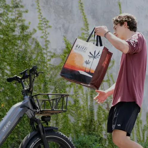 Adolescent posant son sac sur le porte-bagages d’un vélo cargo blanc Yükargo devant un mur végétalisé, illustrant l’expérience Yükargo