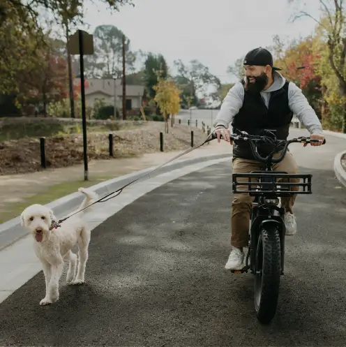 Homme souriant sur son vélo cargo électrique noir Yükargo promenant son chien en laisse dans son quartier