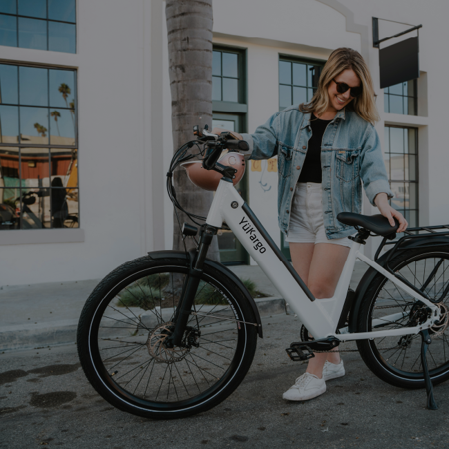 Femme souriante avec lunettes de soleil à côté de son vélo cargo électrique blanc Yükargo devant un immeuble