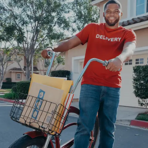 Homme en jean et tee-shirt rouge poussant un vélo cargo rouge Yükargo chargé de courrier, illustrant l’expérience Yükargo