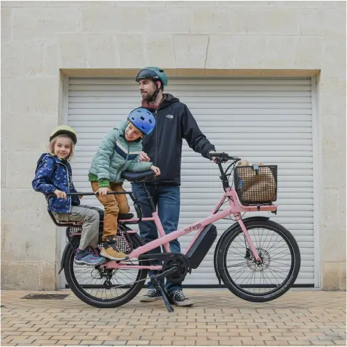 Père de famille avec ses enfants sur un vélo cargo électrique rose Yükargo devant son garage