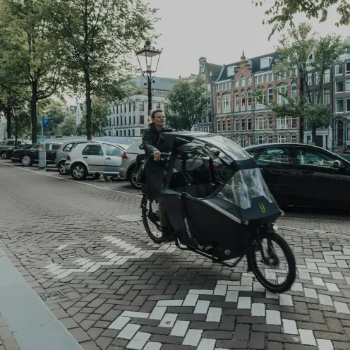 Homme conduisant un vélo cargo électrique noir Yükargo équipé d’un protège-pluie en centre-ville