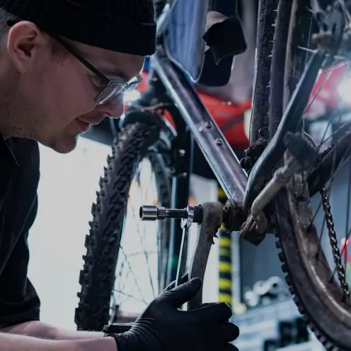 Homme avec bonnet et lunettes réparant un vélo cargo Yükargo en souriant, illustrant l’expérience Yükargo