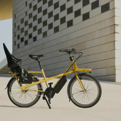 Vélo cargo électrique jaune Yükargo avec siège enfant garé devant un bâtiment moderne