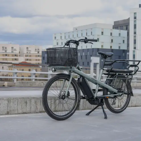 Vélo cargo électrique vert Yükargo à deux roues avec double porte-bagages garé devant des immeubles